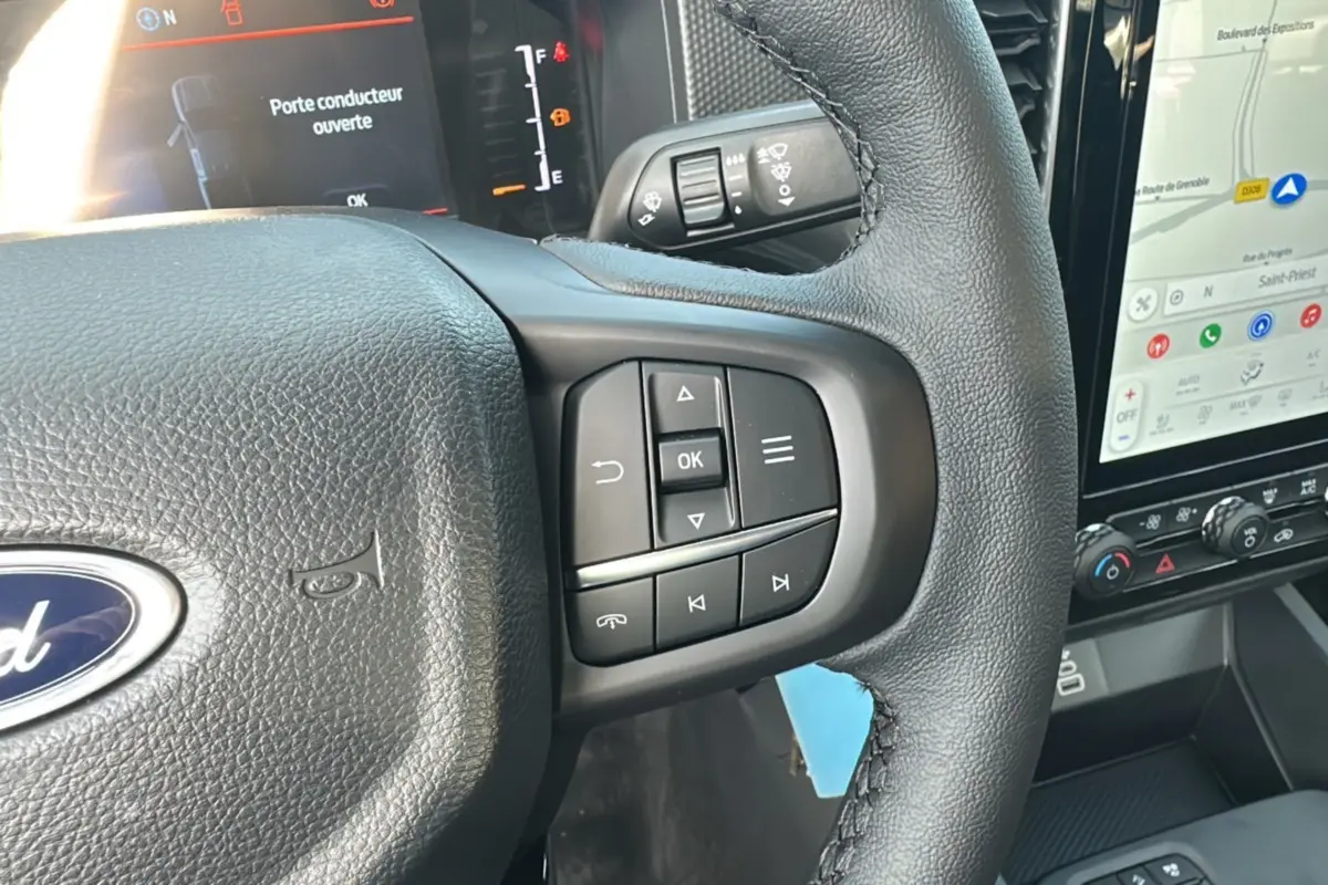 Gros plan sur le volant cuir noir du Ford Ranger 2026 avec commandes multifonctions et écran tactile de navigation visible.