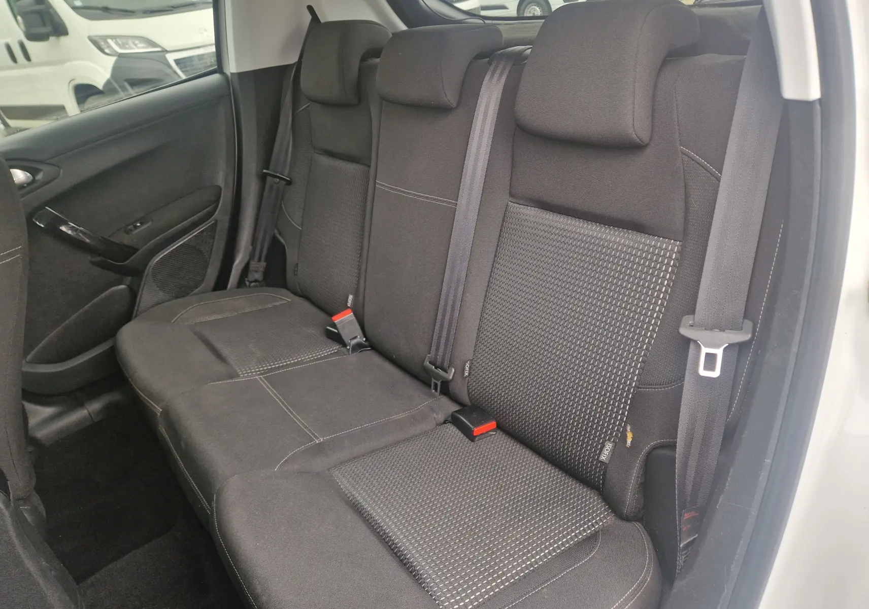 Vue intérieure côté arrière droit montrant la banquette noire avec appuie-têtes et ceintures de sécurité d'une Peugeot 208 blanc nacré.