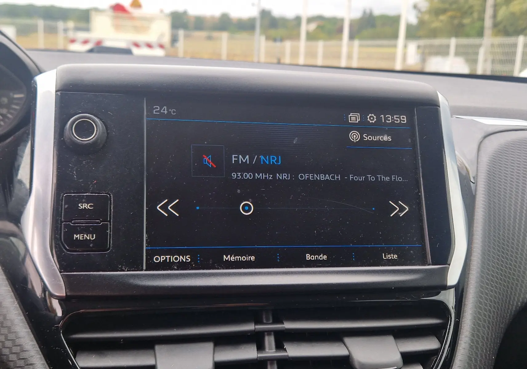 Écran tactile central du tableau de bord de la Peugeot 208 blanc nacré, affichant la radio FM NRJ à 13h59.