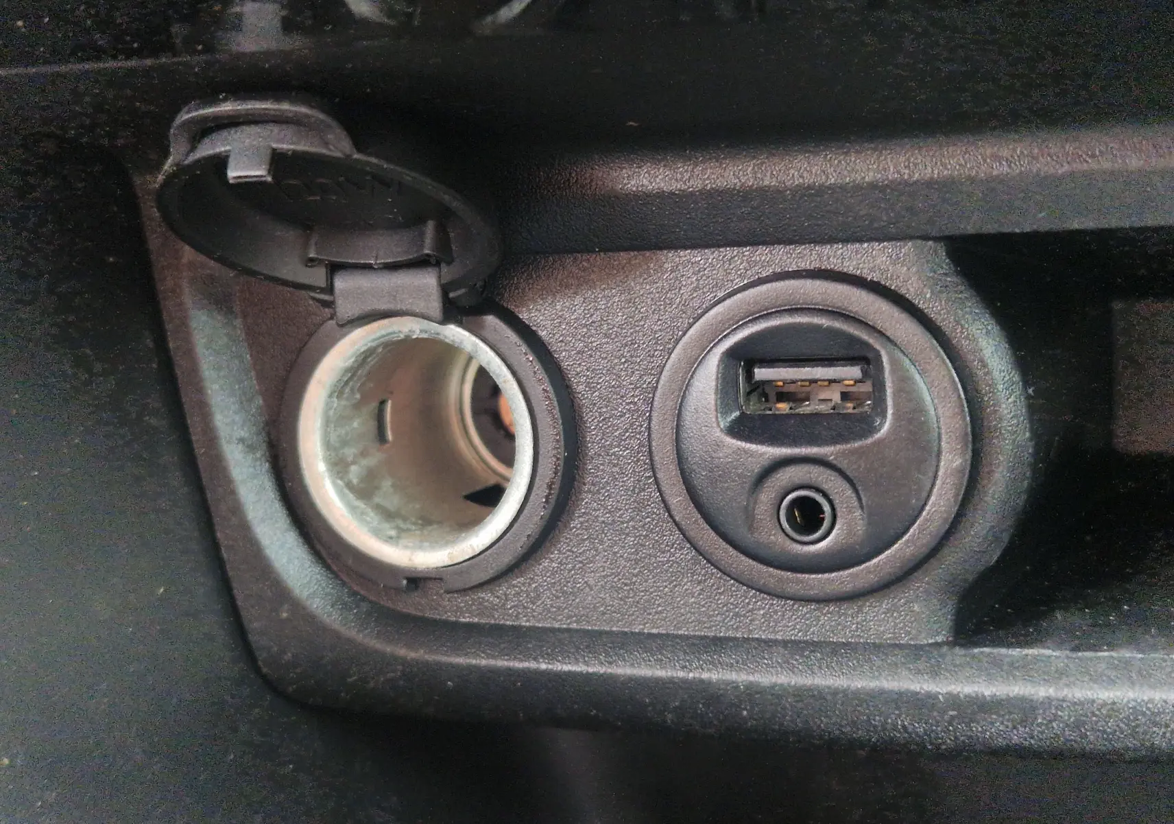 Prise allume-cigare ouverte et port USB avec entrée auxiliaire sur la console centrale d'une Peugeot 208 blanche nacrée.