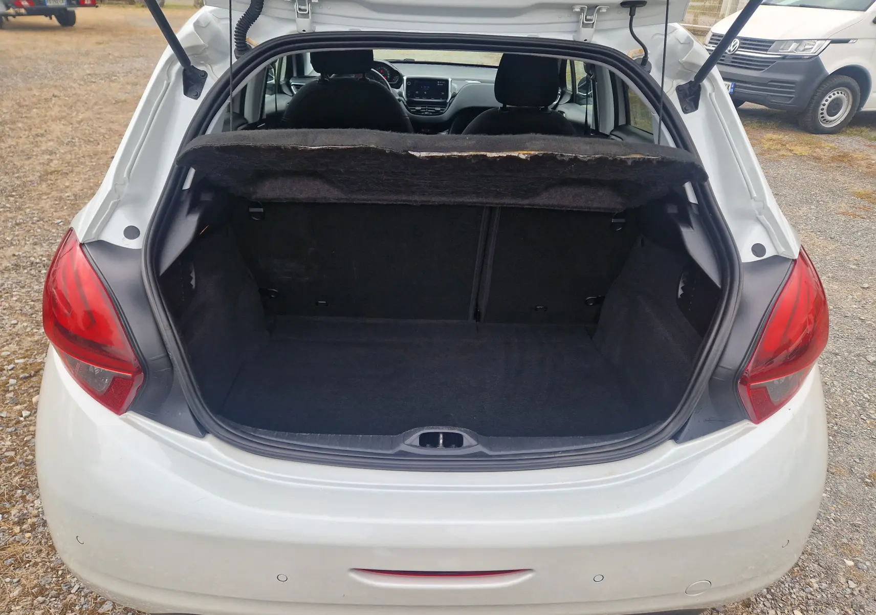 Coffre ouvert vu de l’arrière d’une Peugeot 208 blanc nacré, intérieur noir et banquette arrière visible.