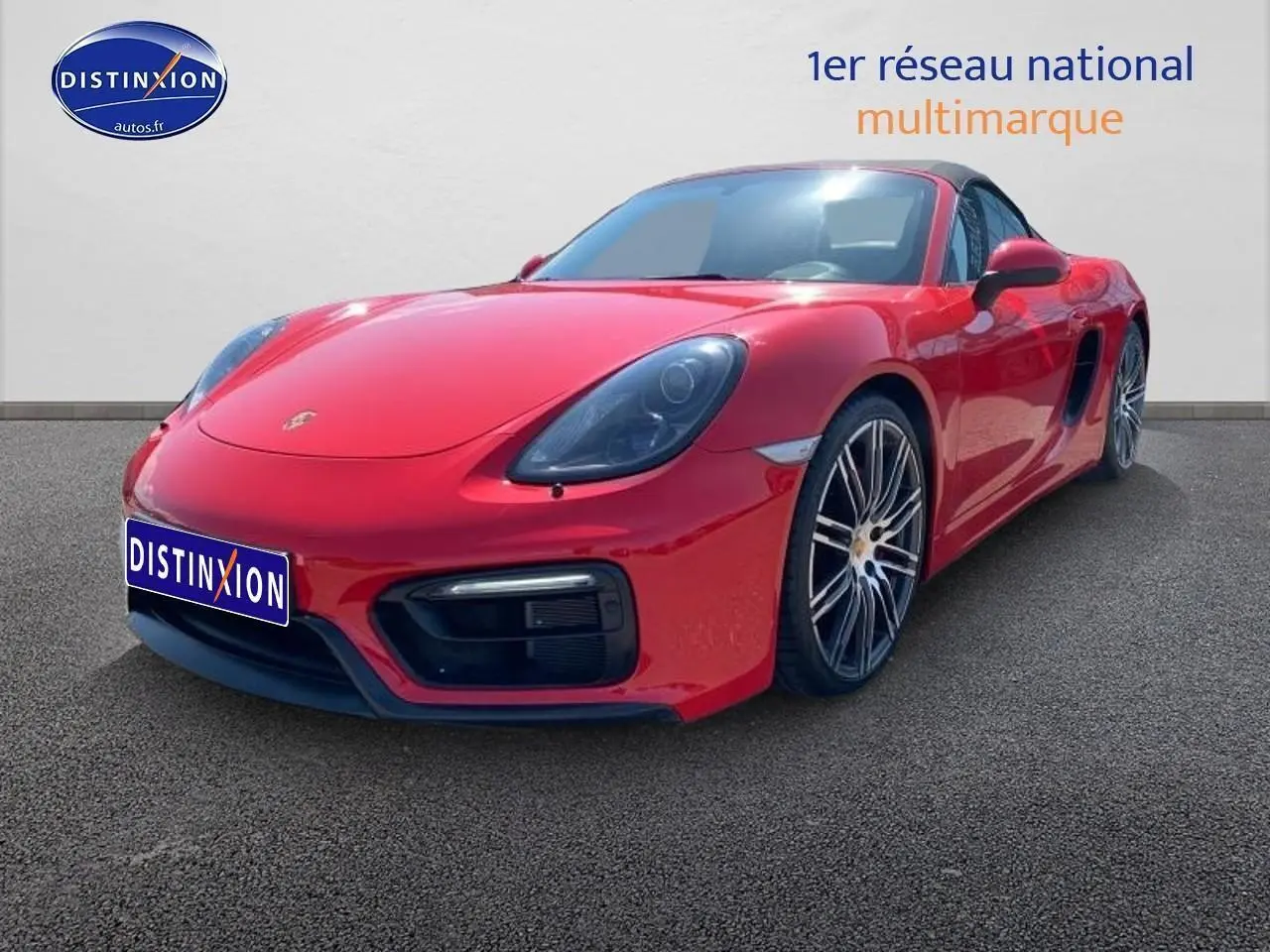 Vue 3/4 avant droite d'une Porsche Boxster rouge (981) avec jantes alu noires et becquet arrière visible.