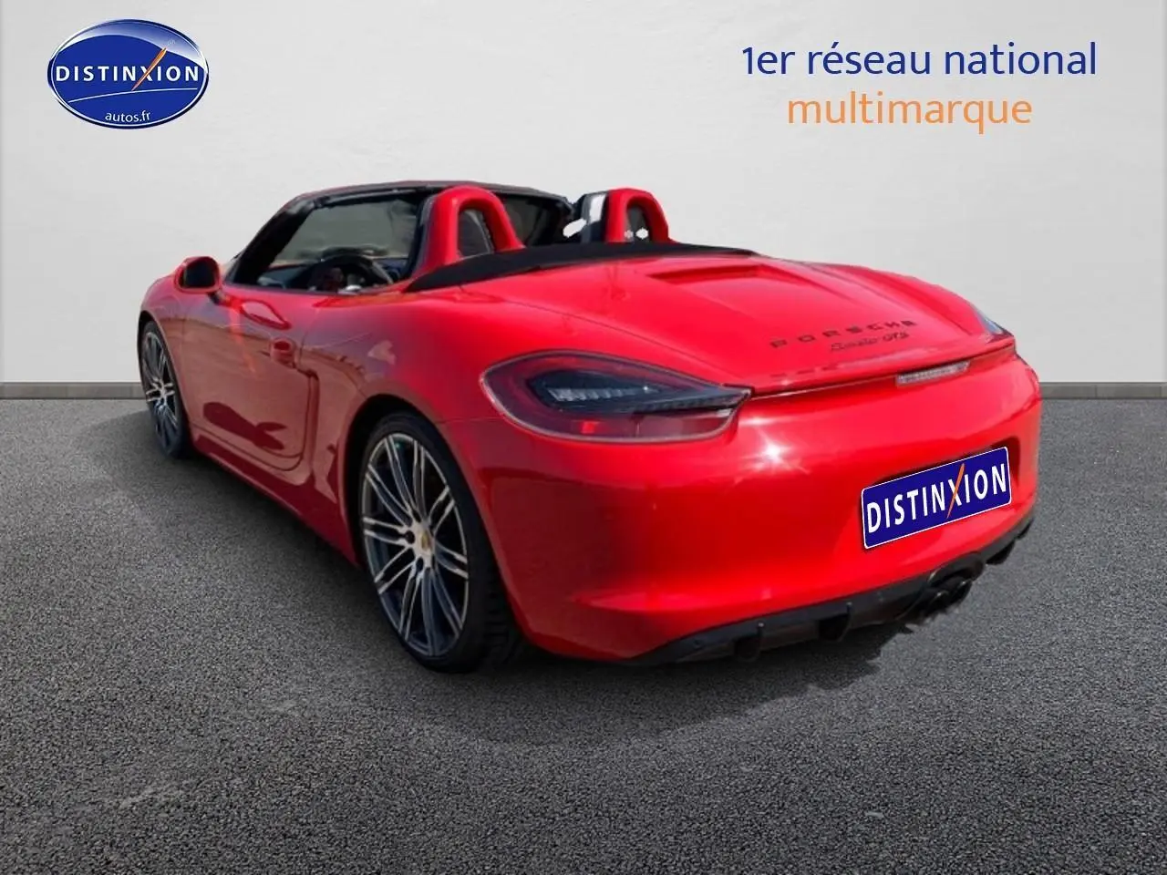 Vue 3/4 arrière droite d'une Porsche Boxster 981 rouge avec capote ouverte et jantes alu multibranches.