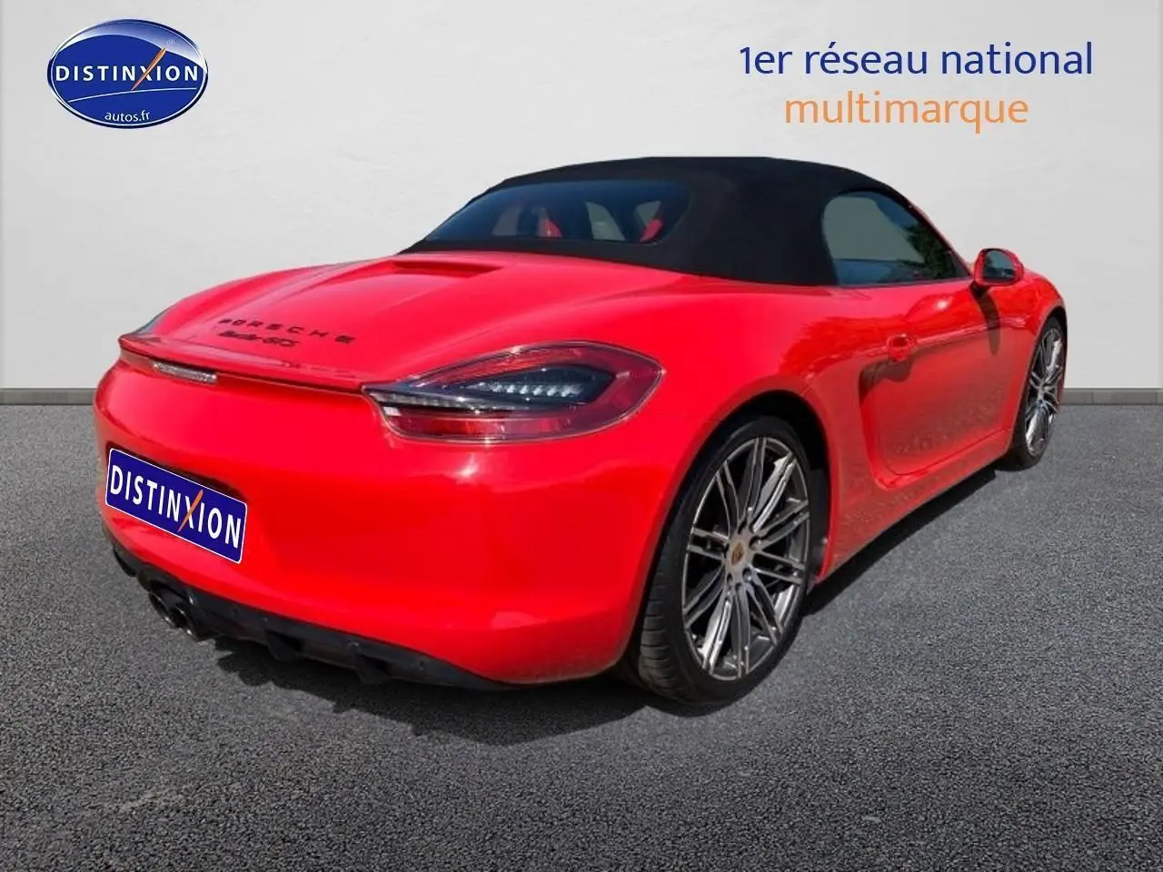 Vue 3/4 arrière droite d'une Porsche Boxster 981 rouge avec capote noire et jantes alu sport