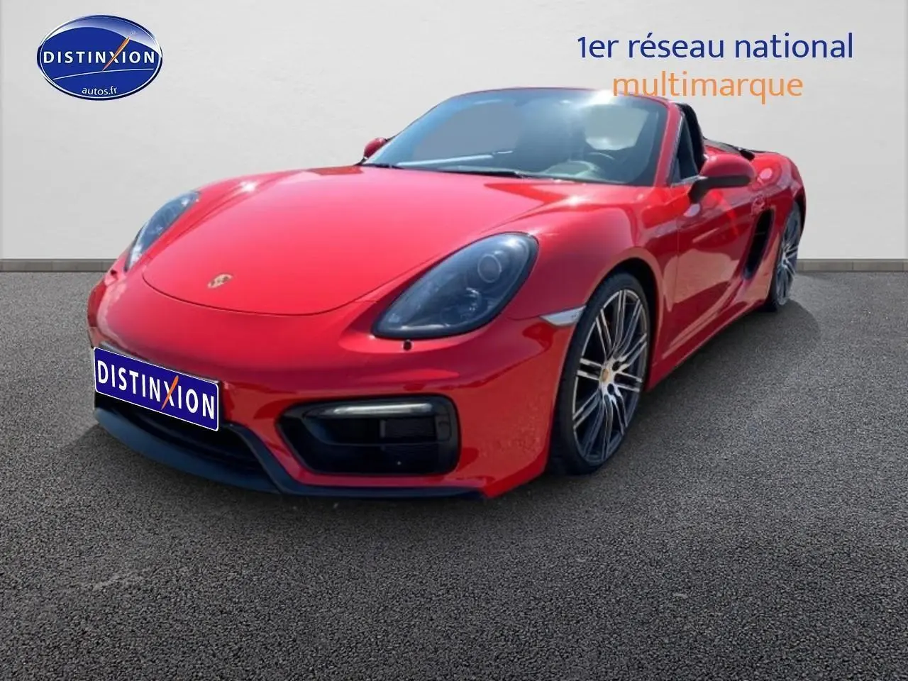 Vue 3/4 avant droite d'une Porsche Boxster 981 rouge avec jantes alu et capote ouverte sur fond neutre.