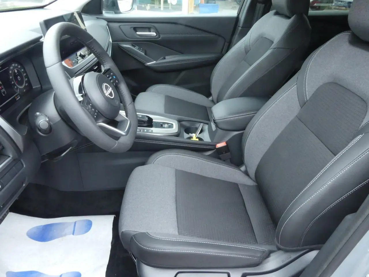 Vue intérieure côté conducteur du Nissan Qashqai 2025 avec sièges tissu gris et volant cuir noir.