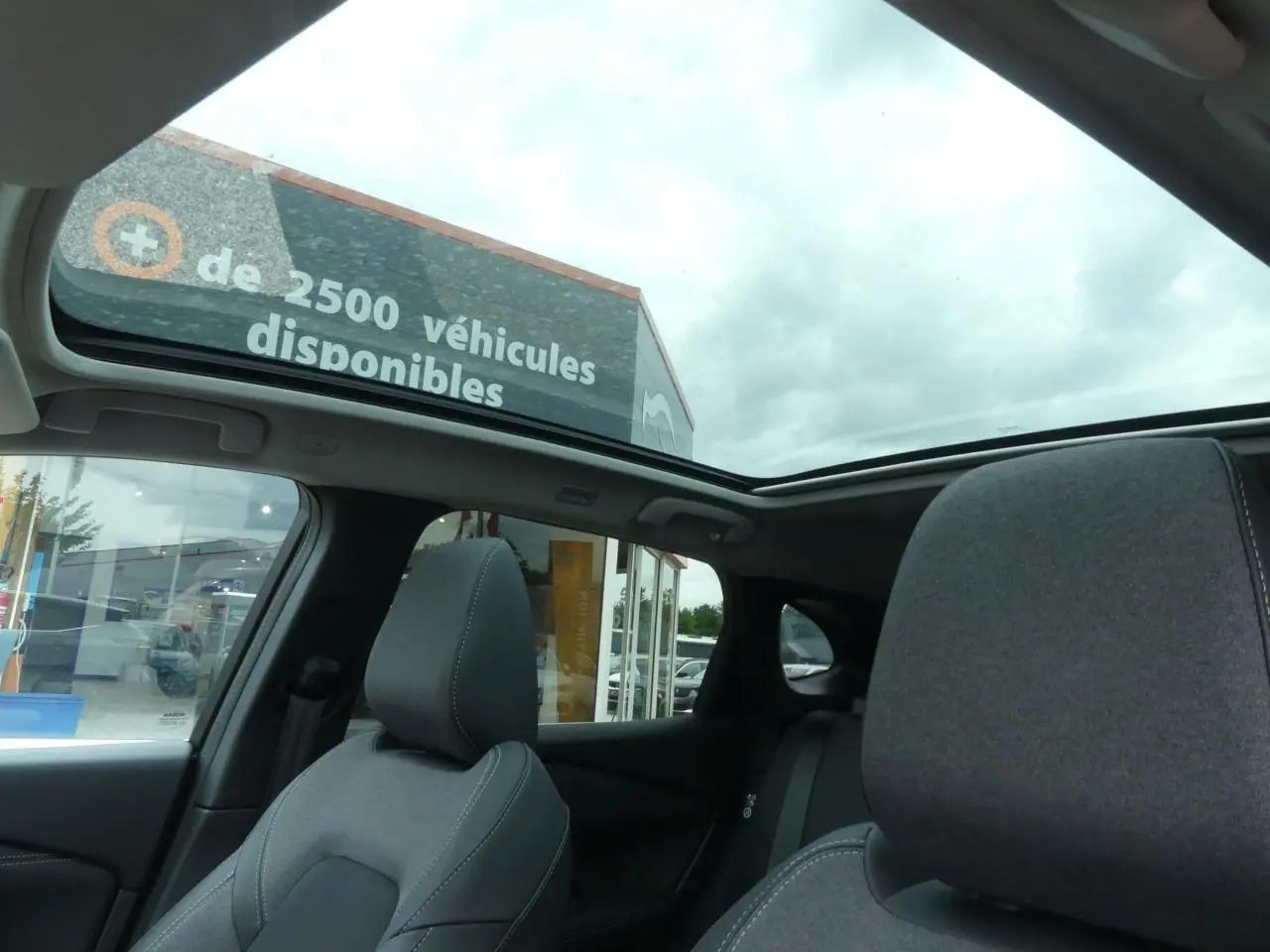 Vue intérieure du toit panoramique en verre du Nissan Qashqai gris métallisé avec sièges avant en tissu gris.