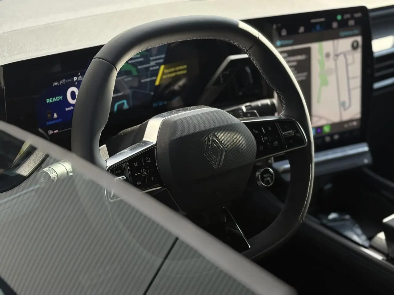 Vue rapprochée du volant en textile et Alcantara avec logo Renault, tableau de bord numérique et écran tactile du Renault Rafale E-Tech.