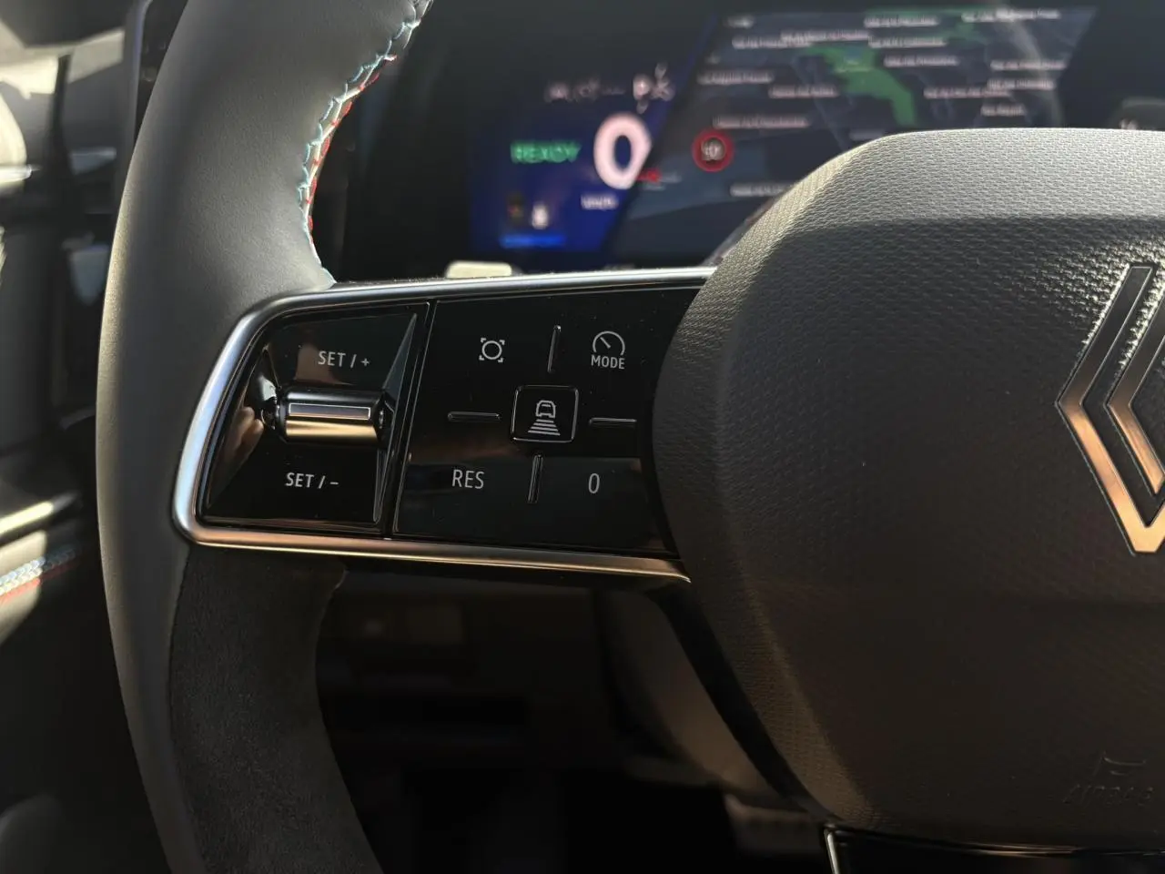 Gros plan sur le volant à droite avec commandes de régulateur, surpiqûres tricolores et logo Renault du Renault Rafale E-Tech.