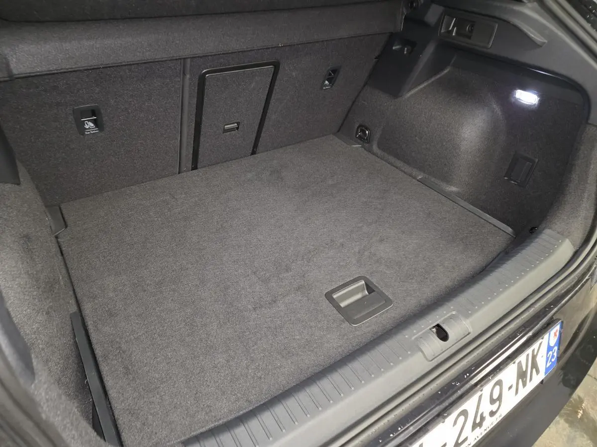 Coffre ouvert vu de l'arrière d'un CUPRA Formentor noir, avec tapis de sol gris et éclairage intérieur.