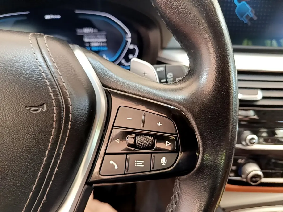 Gros plan sur le volant cuir noir de la BMW Série 5 Touring 530e 2022, avec commandes multifonctions et tableau de bord numérique.