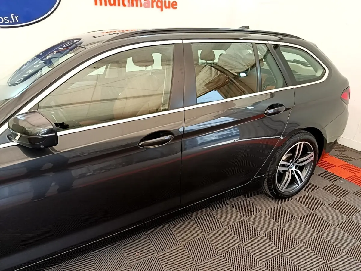 Vue latérale droite d'une BMW Série 5 Touring 530e gris clair avec jantes alliage et rails de toit noirs.
