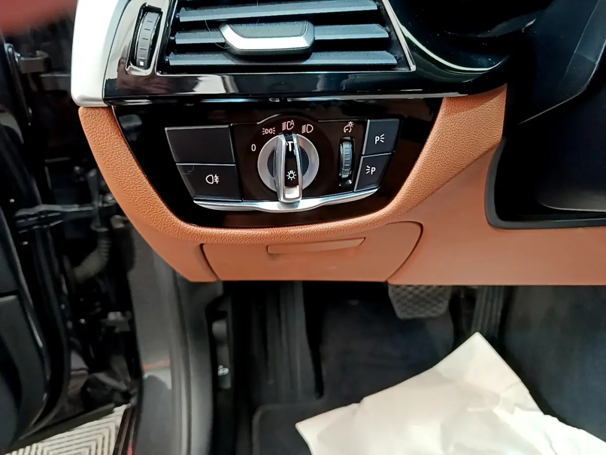 Détail intérieur du panneau de commande des phares sur tableau de bord marron clair d'une BMW Série 5 Touring 530e.