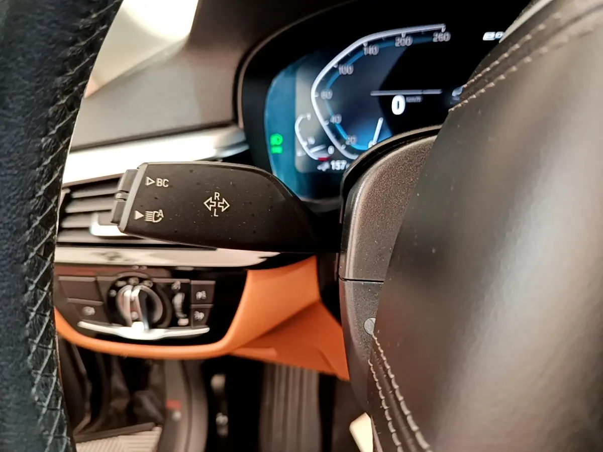 Gros plan sur le volant noir et le tableau de bord numérique bleu de la BMW Série 5 Touring 530e 2022.