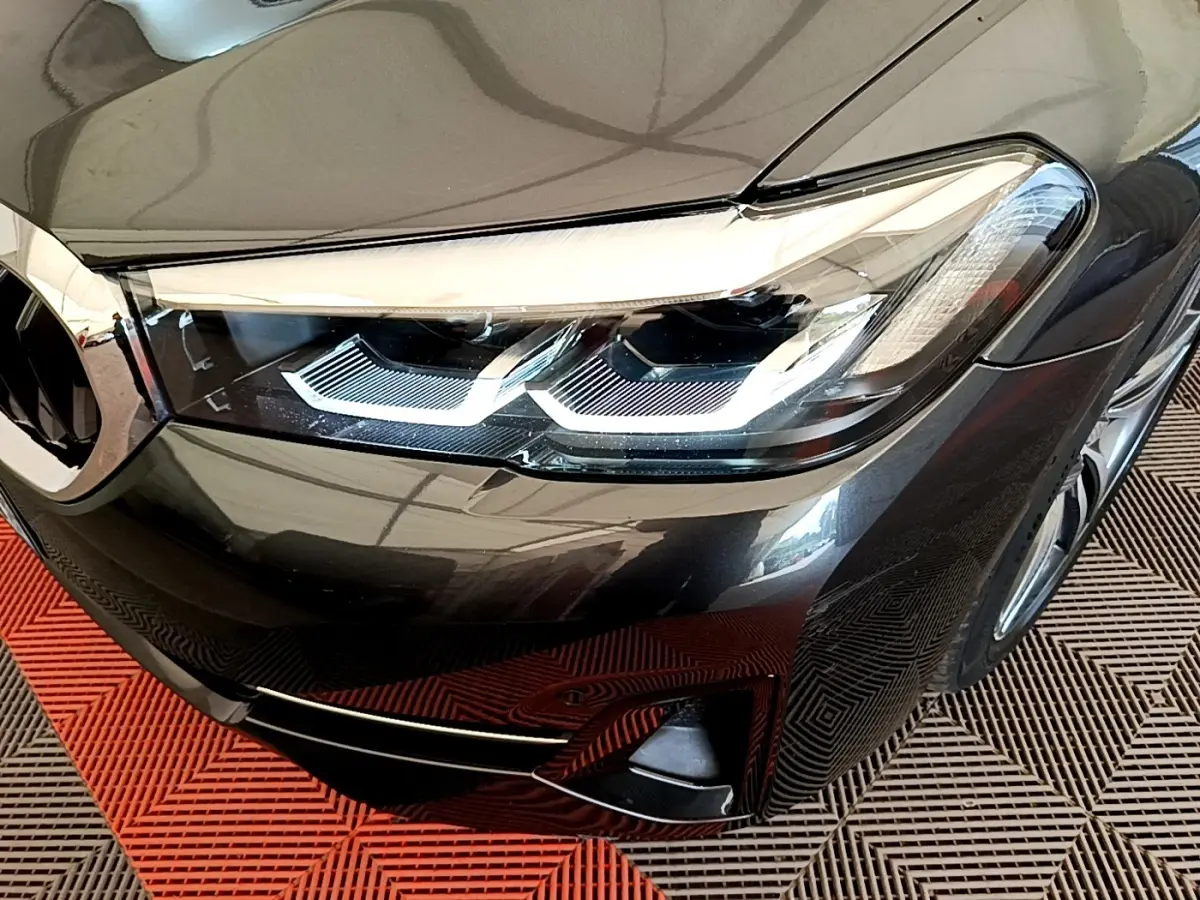 Gros plan sur le phare avant droit d'une BMW Série 5 Touring gris clair avec détails LED et calandre partielle visible.