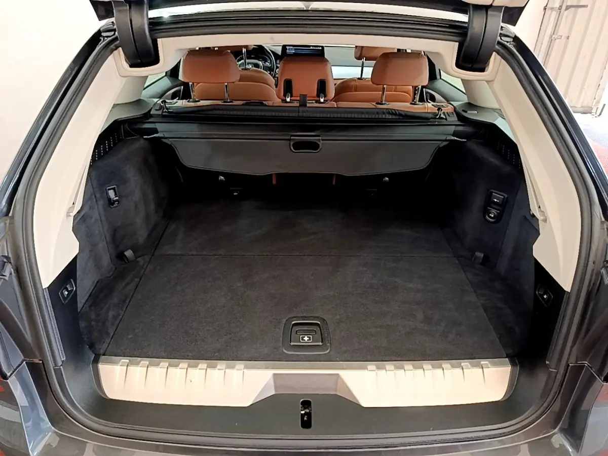Vue arrière du coffre spacieux d'une BMW Série 5 Touring 530e gris clair avec sièges arrière en cuir marron.