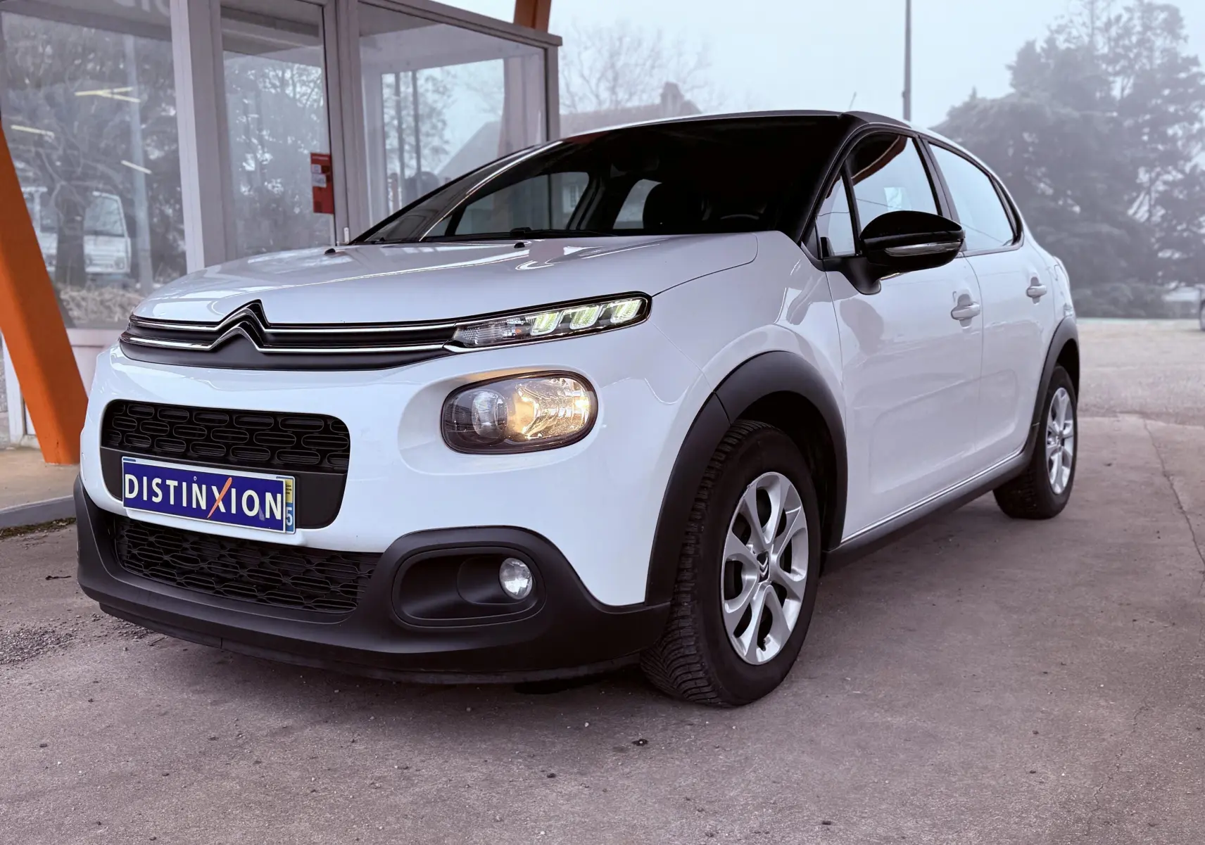 Vue 3/4 avant droite d'une Citroën C3 Société blanche de 2019 avec calandre noire et feux allumés.