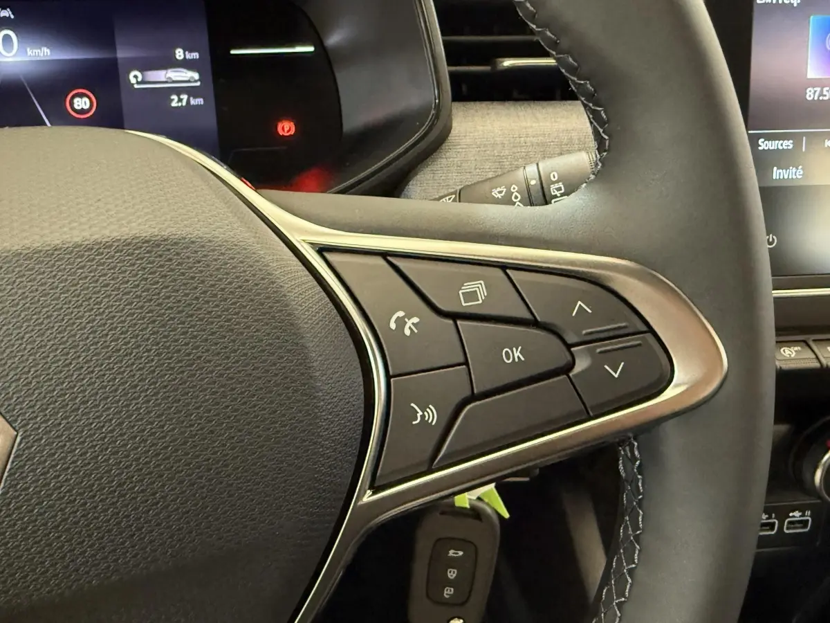 Gros plan sur le volant cuir noir de la Renault Clio 2025 avec commandes multifonctions et affichage numérique partiel.