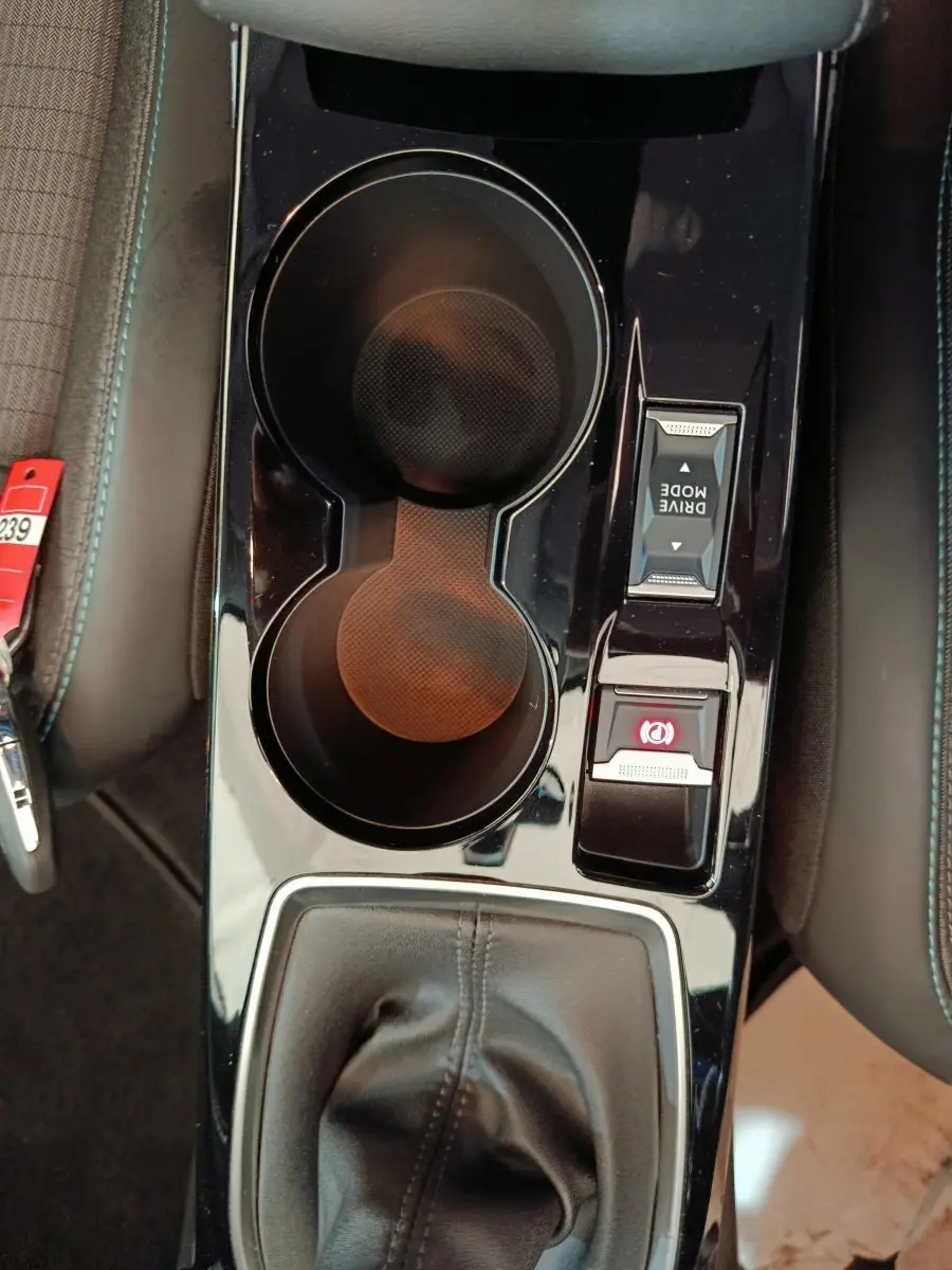 Vue plongeante sur la console centrale noire brillante de la Peugeot 208 avec porte-gobelets et commandes Drive Mode et frein électrique.