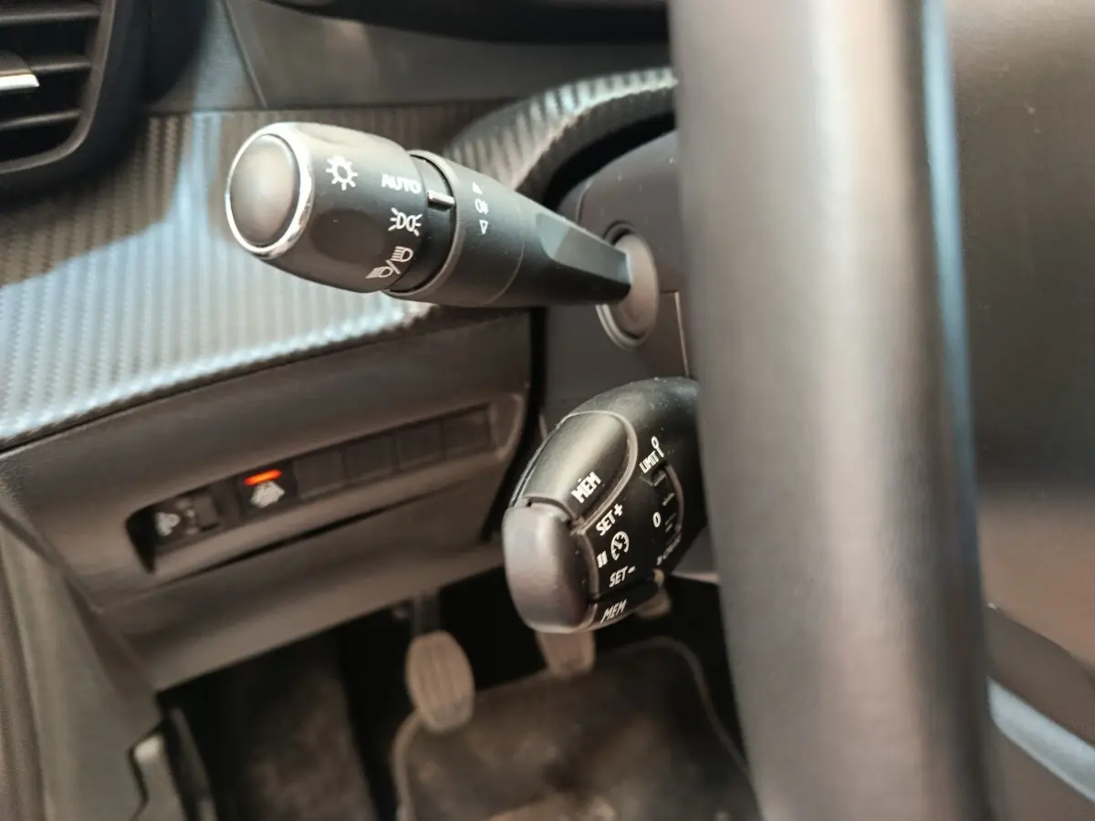 Gros plan sur la commande de régulateur de vitesse et les commandes d’éclairage derrière le volant noir du Peugeot 208.