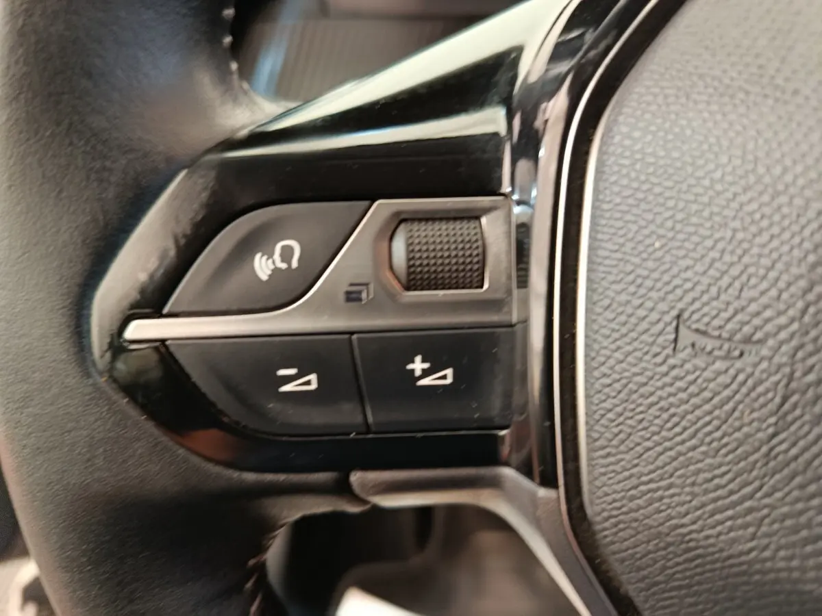 Gros plan sur les commandes multifonctions en cuir du volant gauche d'une Peugeot 208 2020, finition Allure Business.
