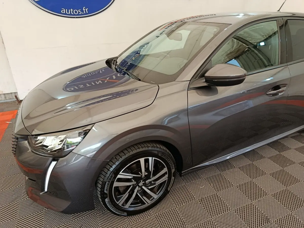 Vue 3/4 avant droit d'une Peugeot 208 gris métallisé avec phares LED et jantes alliage distinctives.