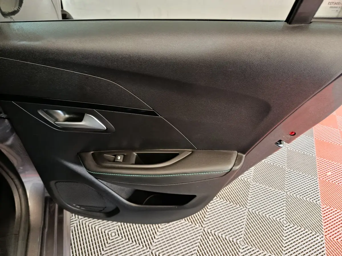 Vue rapprochée du panneau de porte intérieur côté gauche de la Peugeot 208 2020, finition noire avec surpiqûres vertes.