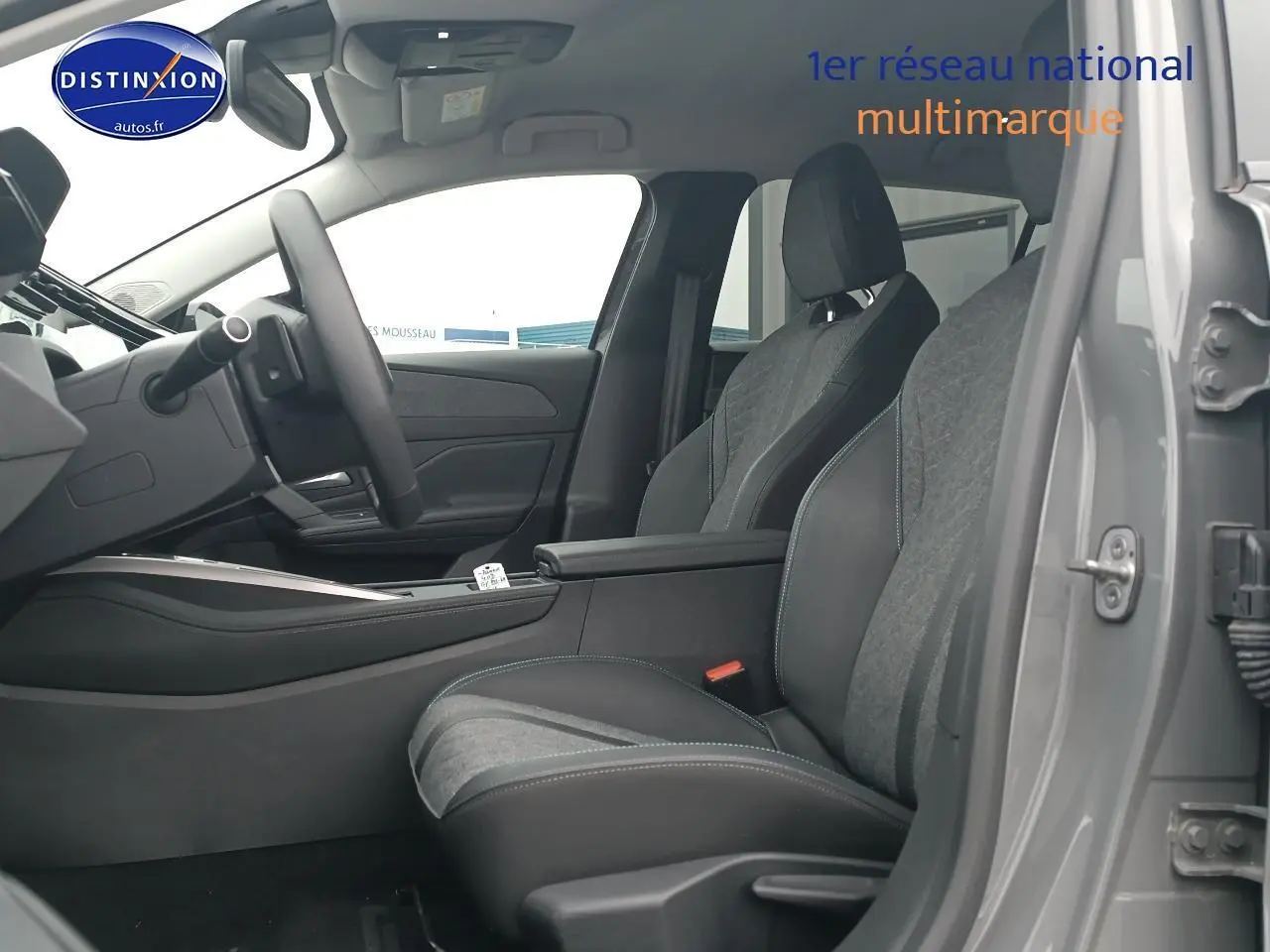 Vue intérieure côté conducteur de la Peugeot 408 Hybrid gris sellenium, avec sièges bi-matière et accoudoir central ouvert.