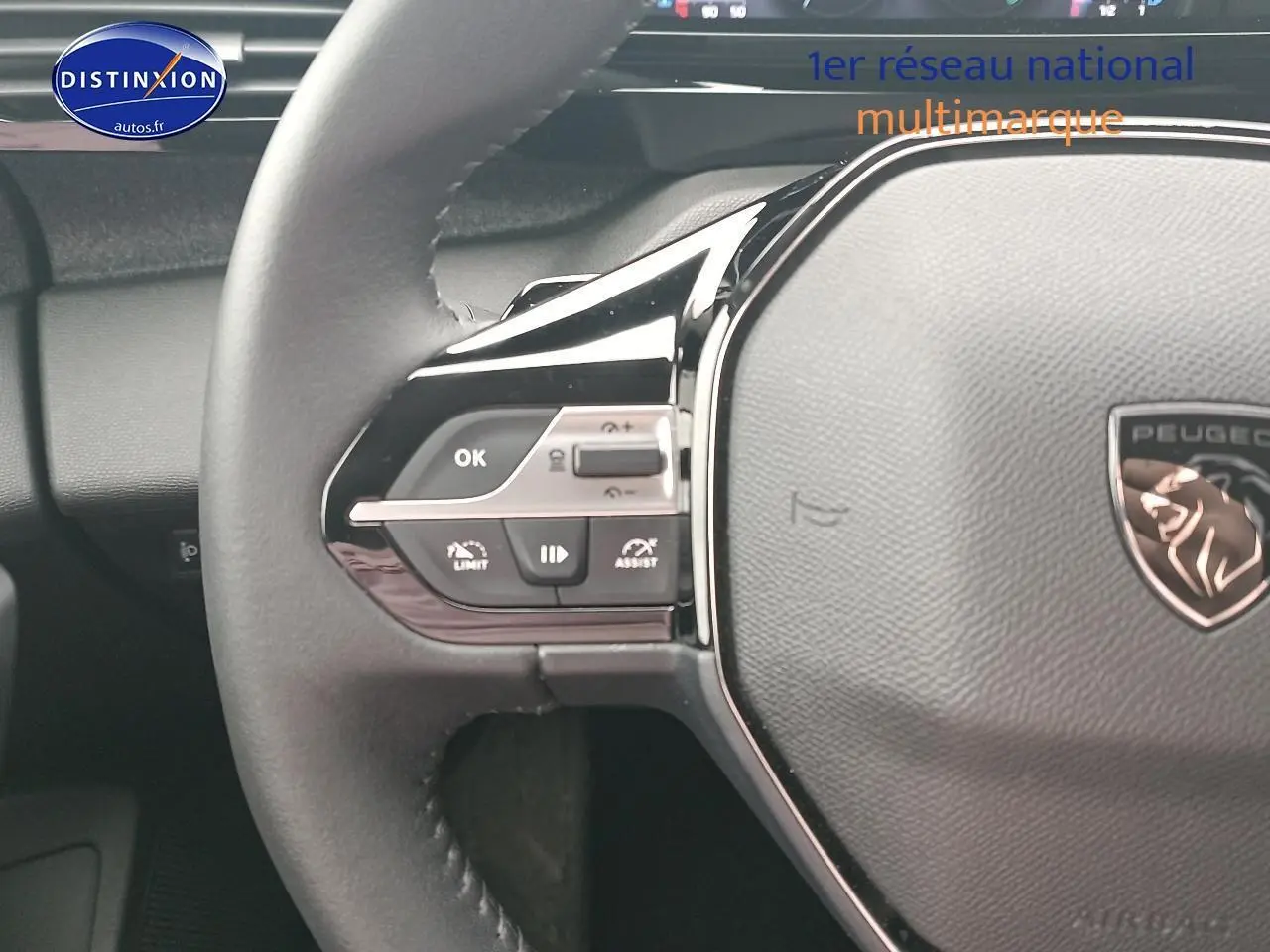 Gros plan sur le volant cuir multifonction gris d’une Peugeot 408 Hybrid 145 allure 2024 avec commandes intégrées côté gauche.