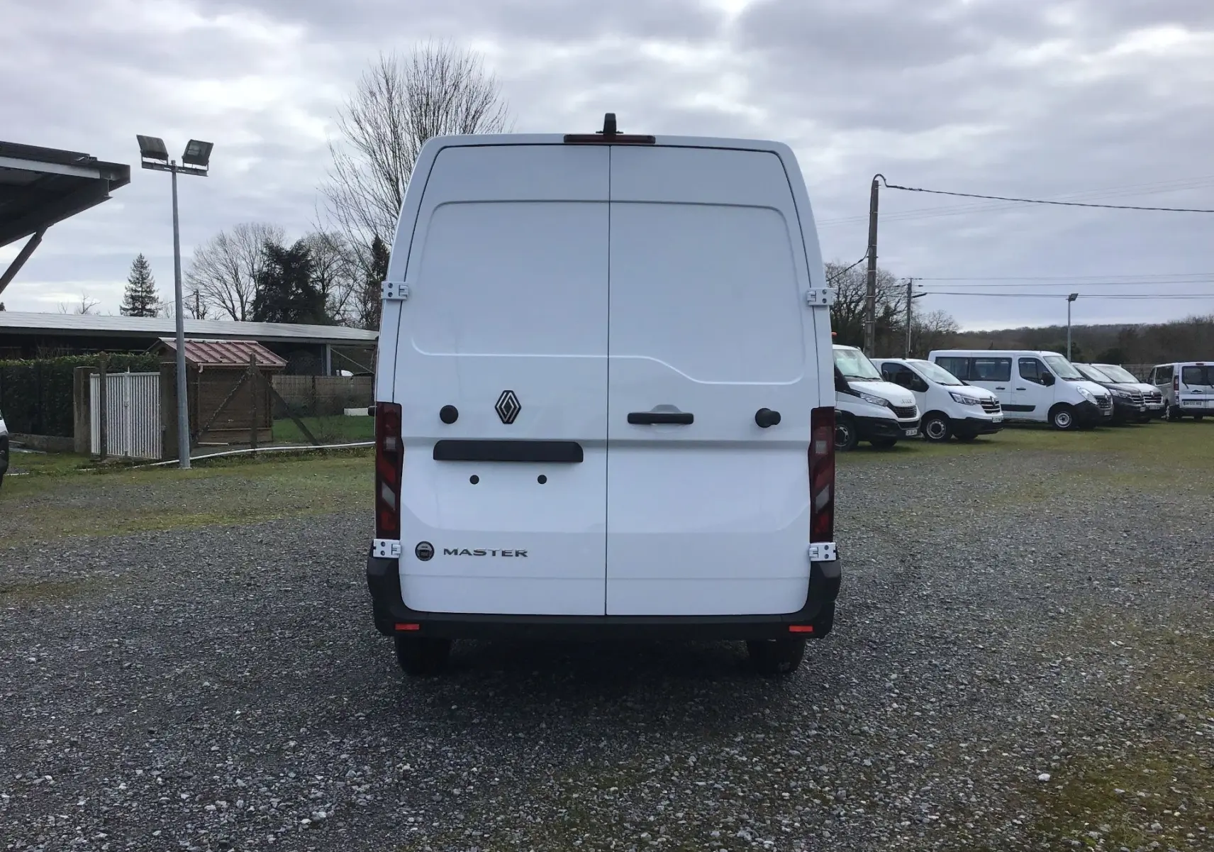 Vue arrière d’un Renault Master blanc L2H2 avec portes battantes fermées sur un terrain extérieur.
