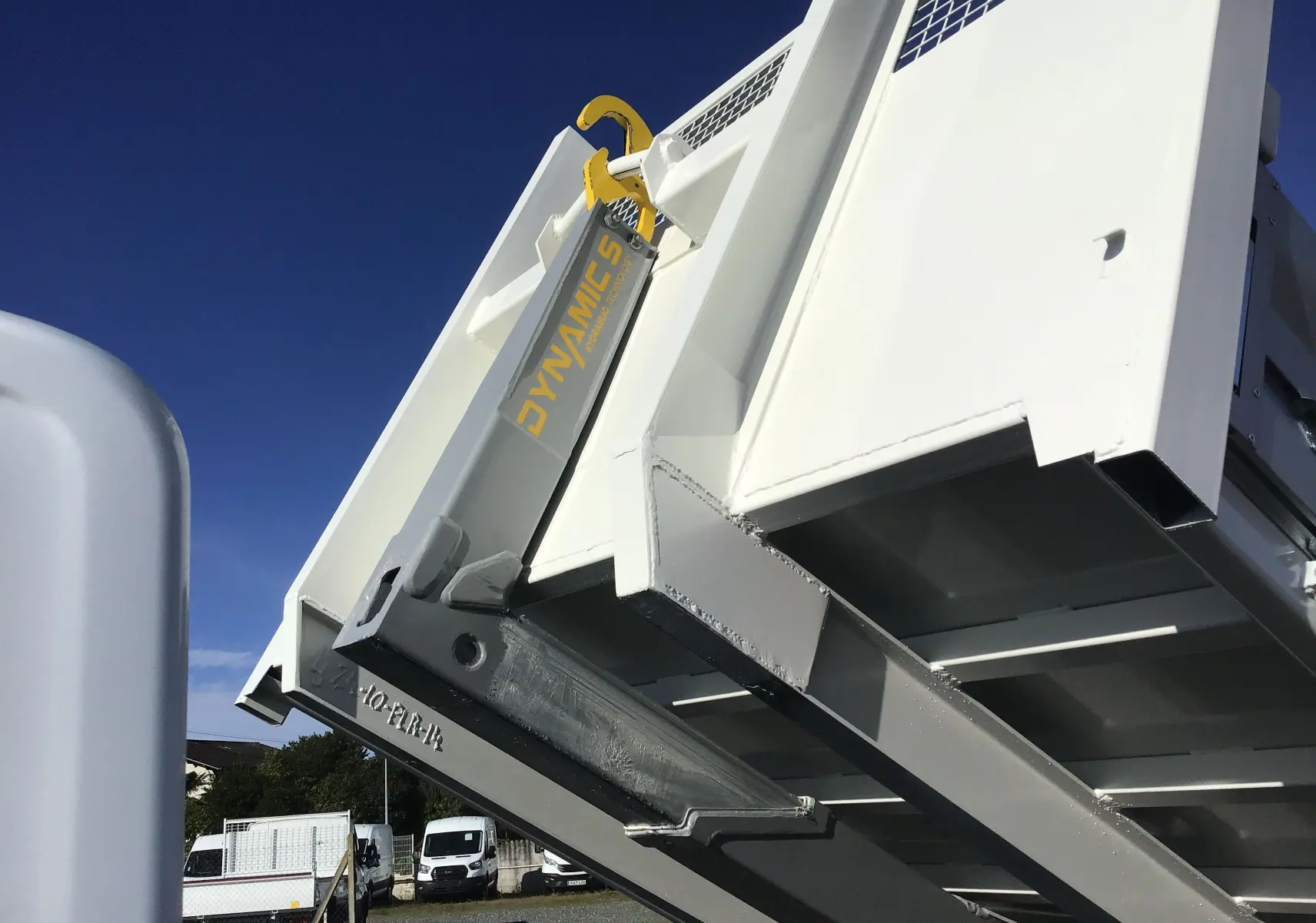 Gros plan sur le bras polybenne blanc relevé du Ford Transit Châssis Cabine, sous un ciel bleu dégagé.