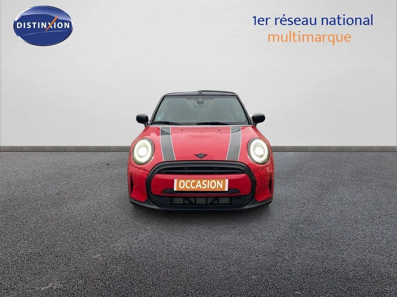 Vue frontale d'une MINI Cabriolet F57 rouge chili avec bandes noires sur le capot et phares allumés.