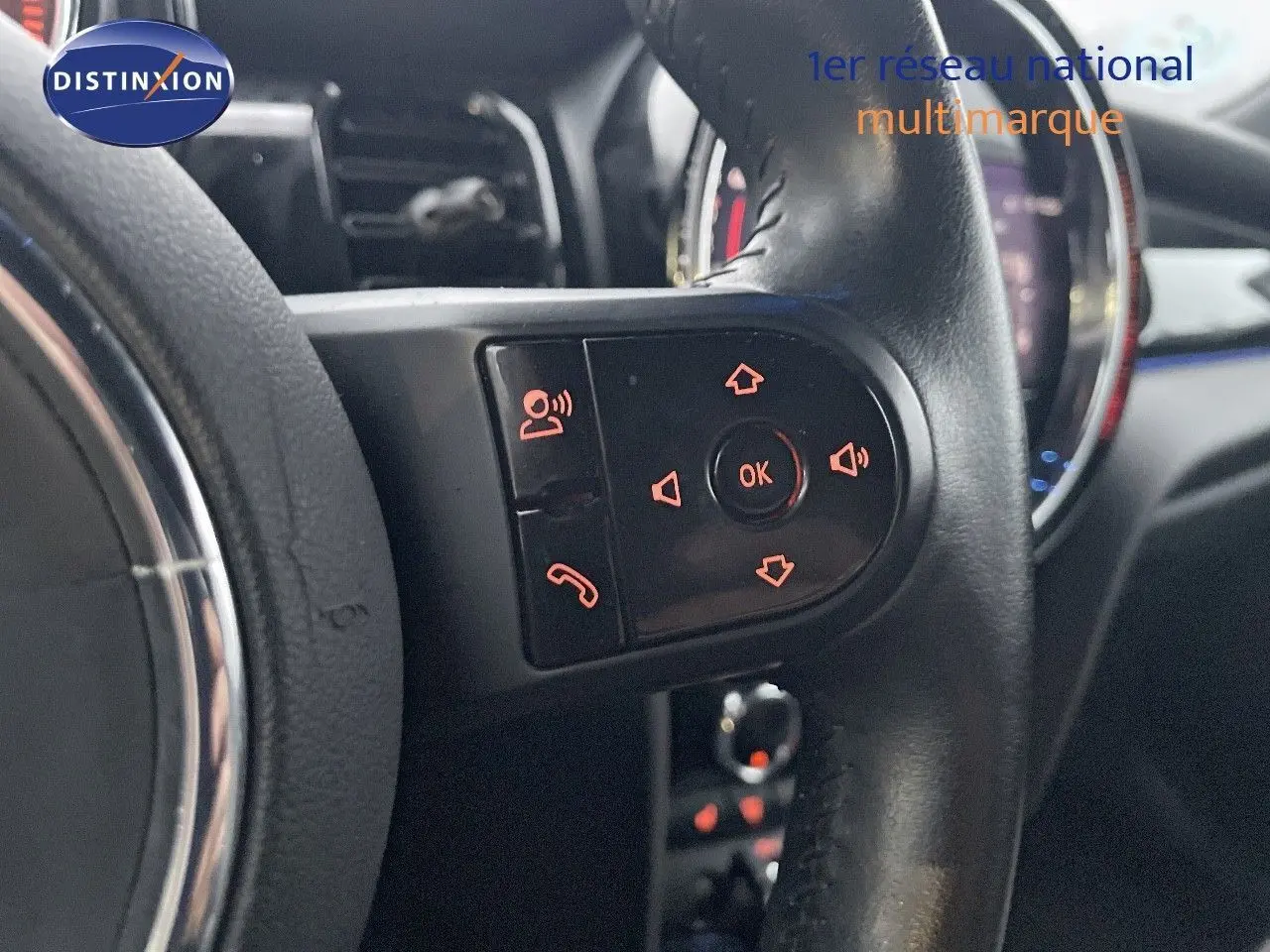 Gros plan sur les commandes du volant noir de la MINI Cabriolet F57 rouge chili, avec boutons rétroéclairés orange.