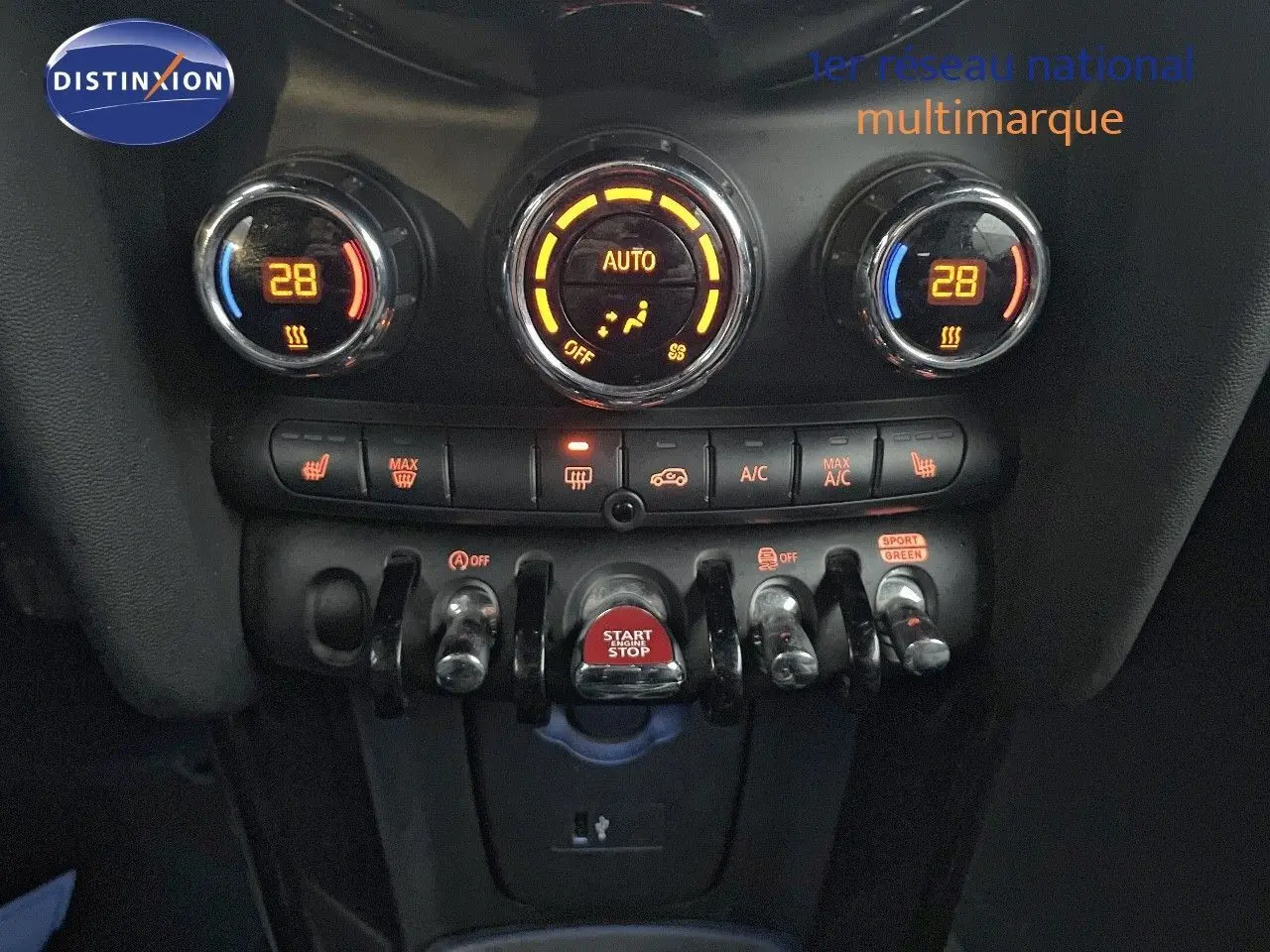 Gros plan sur la console centrale de la MINI Cabriolet rouge chili, montrant les commandes de climatisation et le bouton start/stop.