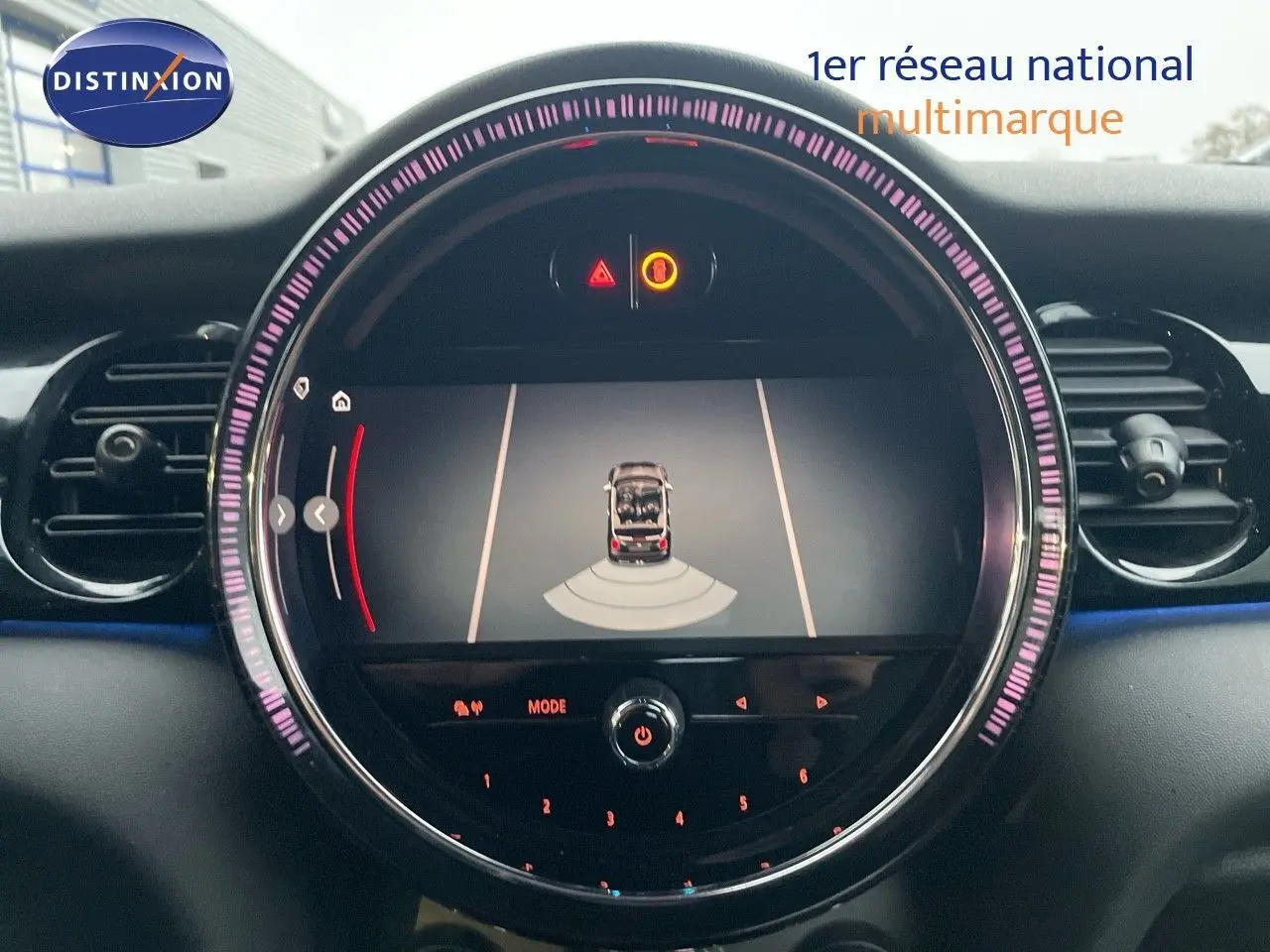 Vue rapprochée de l'écran central du tableau de bord d'une MINI Cabriolet rouge chili, affichant l'aide au stationnement.