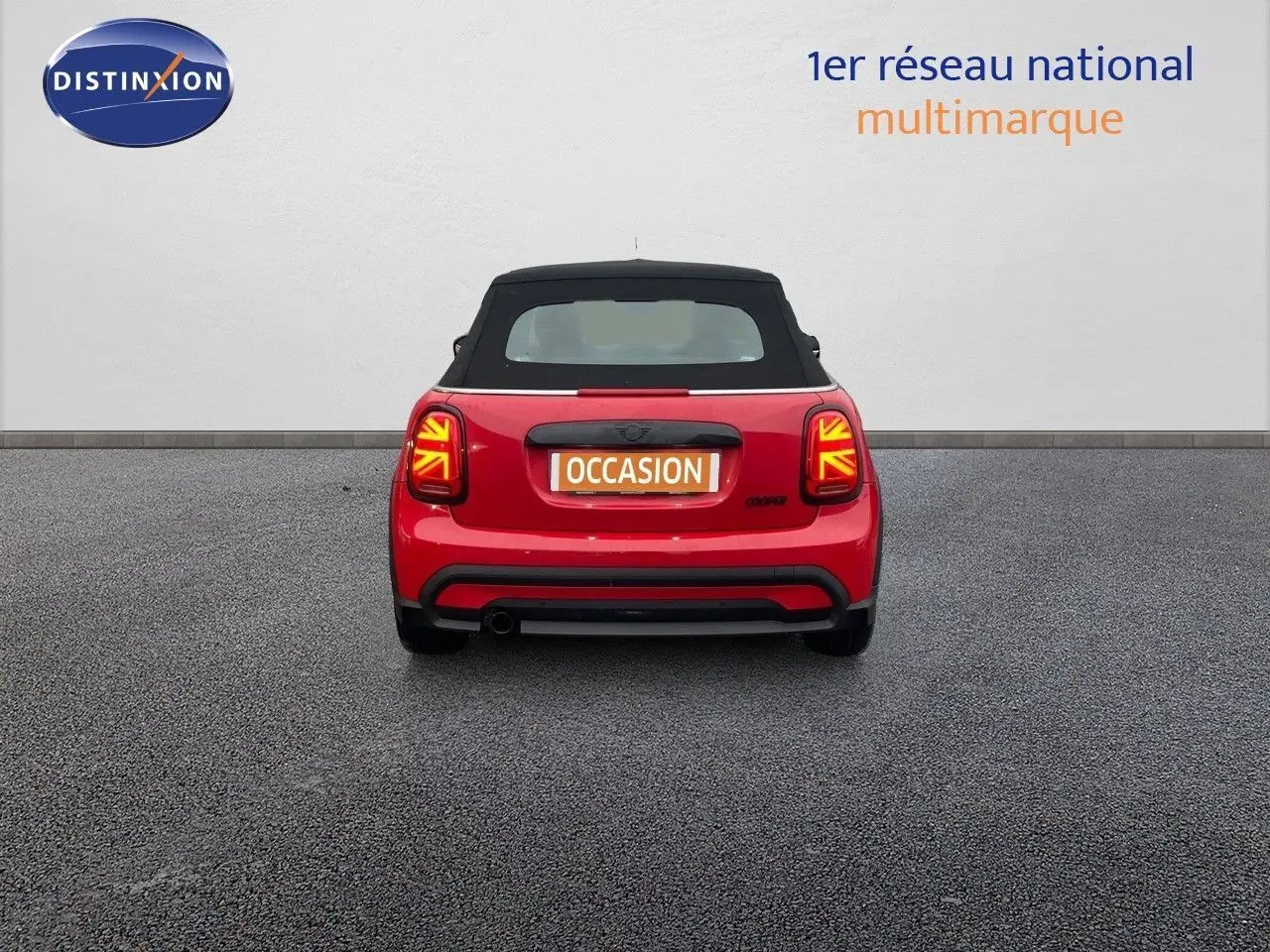 Vue arrière d'une MINI Cabriolet F57 rouge chili avec capote noire et feux arrière à motif Union Jack allumés.