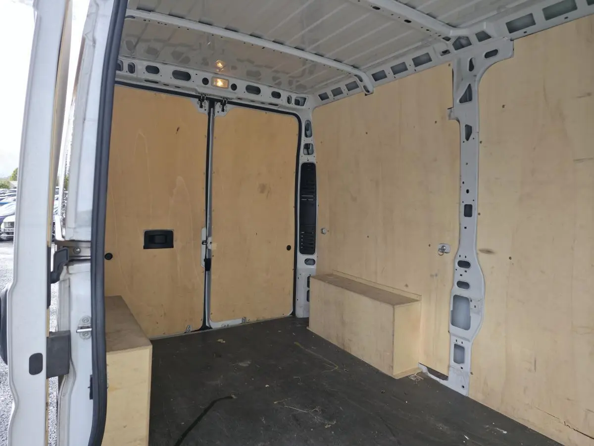 Intérieur du fourgon Opel Movano blanc vu de l'arrière avec panneaux latéraux et plancher en bois clair.