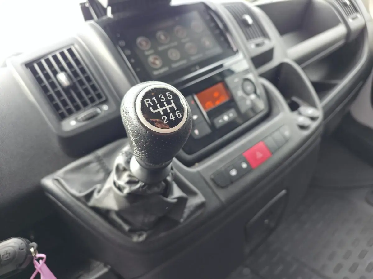 Gros plan sur le levier de vitesses manuel et la console centrale noire de l'intérieur du fourgon Opel Movano blanc.