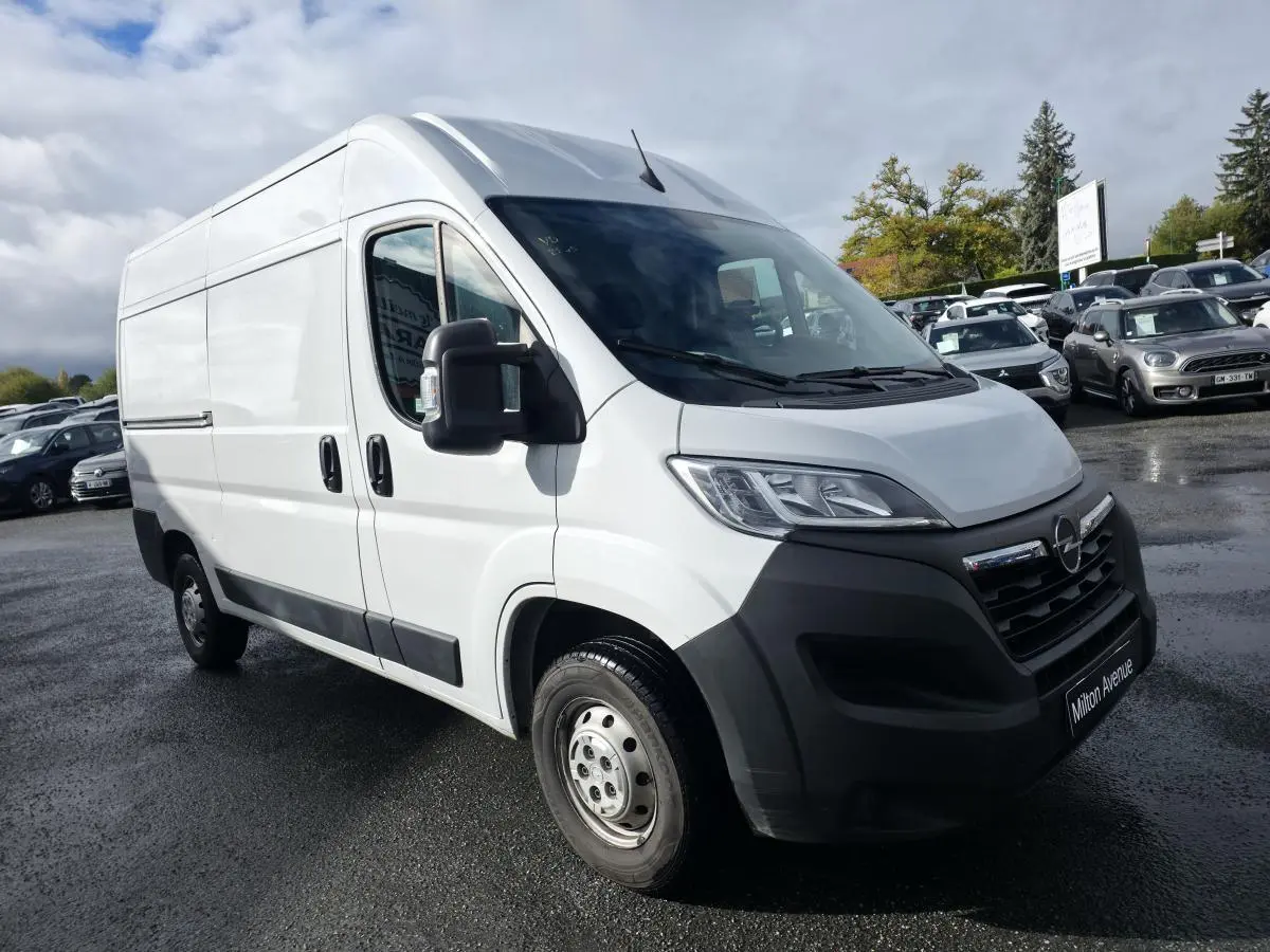 Opel Movano Fourgon blanc vu en 3/4 avant droit avec pare-chocs noir et portes latérales tôlées.
