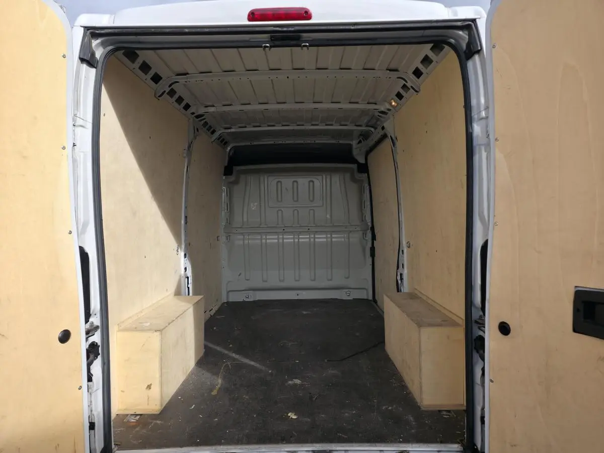 Vue arrière intérieure du fourgon blanc Opel Movano avec panneaux latéraux en bois et plancher noir.