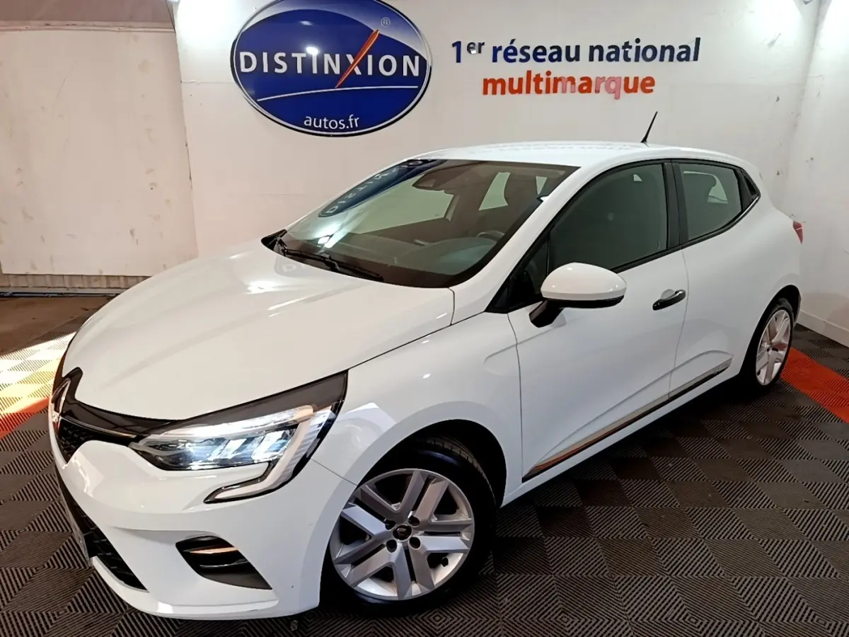 Renault Clio Business blanc vue 3/4 avant droit, feux LED allumés, dans showroom avec logo Distinxion en arrière-plan.