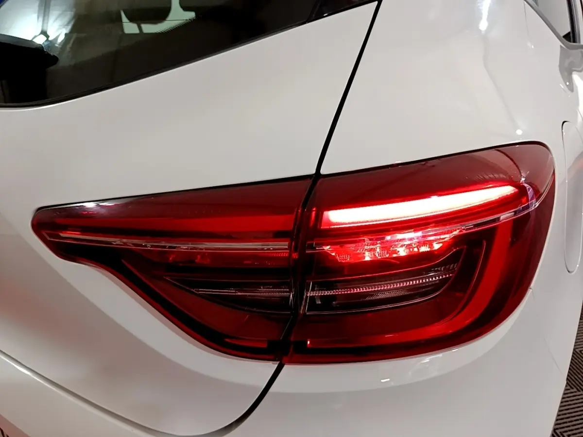 Gros plan sur le feu arrière droit rouge allumé d’une Renault Clio Business blanche, vue arrière côté droit.