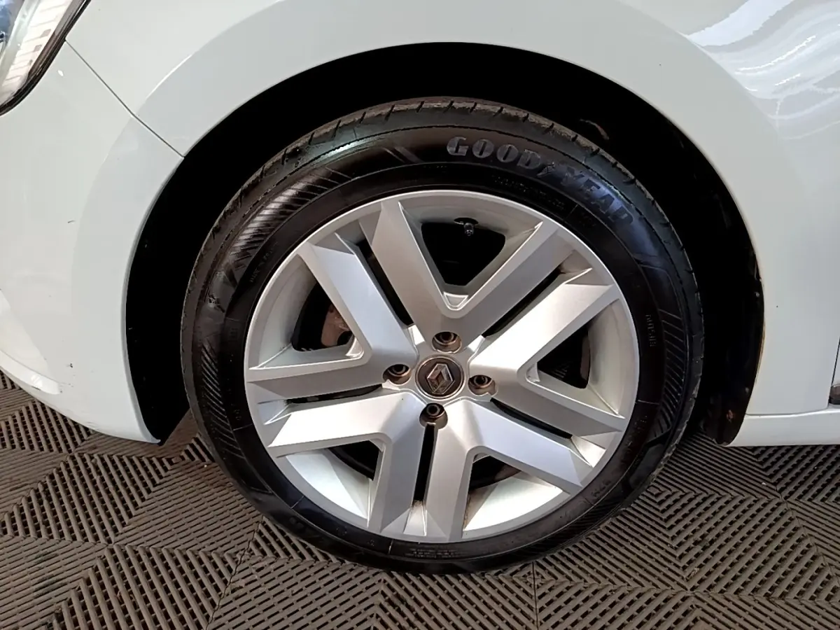 Gros plan sur la roue avant droite avec jante argentée et logo Renault d'une Renault Clio blanche.