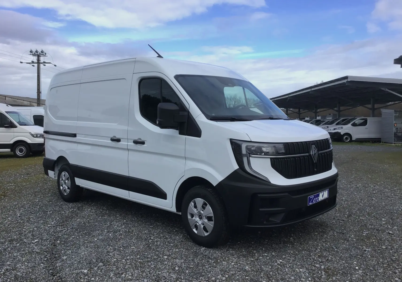 Renault Master blanc en vue 3/4 avant droit, avec calandre noire et pare-chocs noir mat, stationné sur gravier.