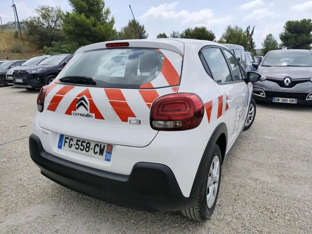Vue 3/4 arrière droite d'une Citroën C3 Société blanche avec bandes rouges diagonales sur le hayon et le côté.