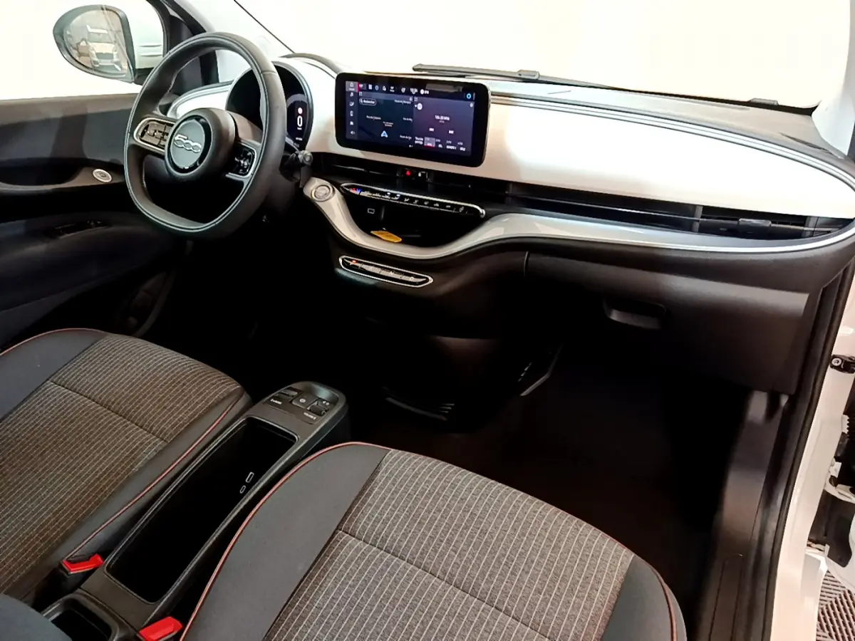 Vue intérieure côté conducteur de la FIAT 500 électrique blanche, tableau de bord moderne avec écran tactile central.