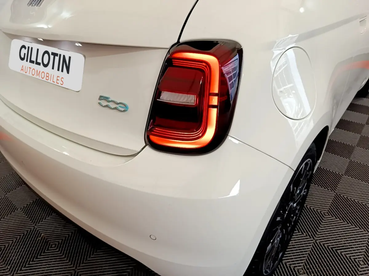 Vue 3/4 arrière droite d'une FIAT 500 blanche électrique avec feu arrière LED distinctif et logo 500 bleu.