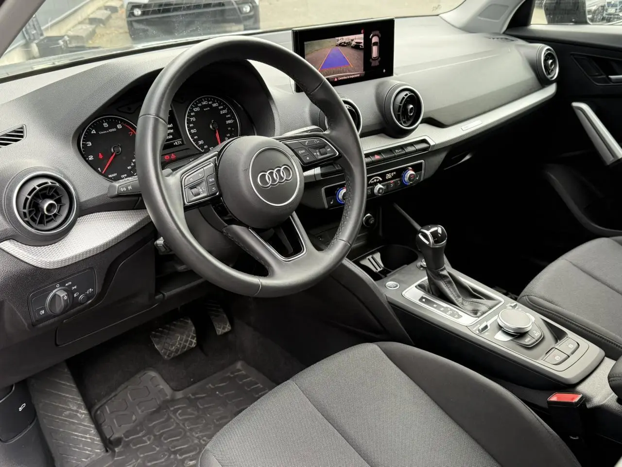 Intérieur de l'Audi Q2 35 TFSI 2023 vu côté conducteur, avec tableau de bord moderne et écran caméra de recul.