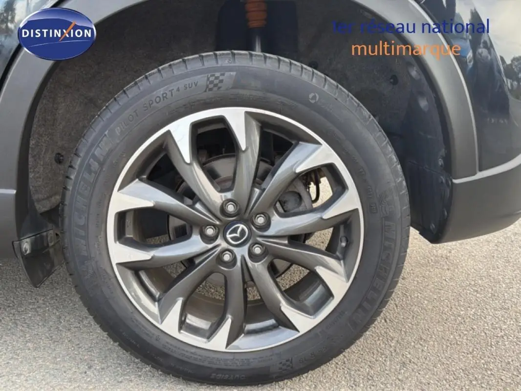 Gros plan sur la jante alliage 19 pouces gris foncé du Mazda CX-5 noir, mettant en valeur le logo Mazda central.