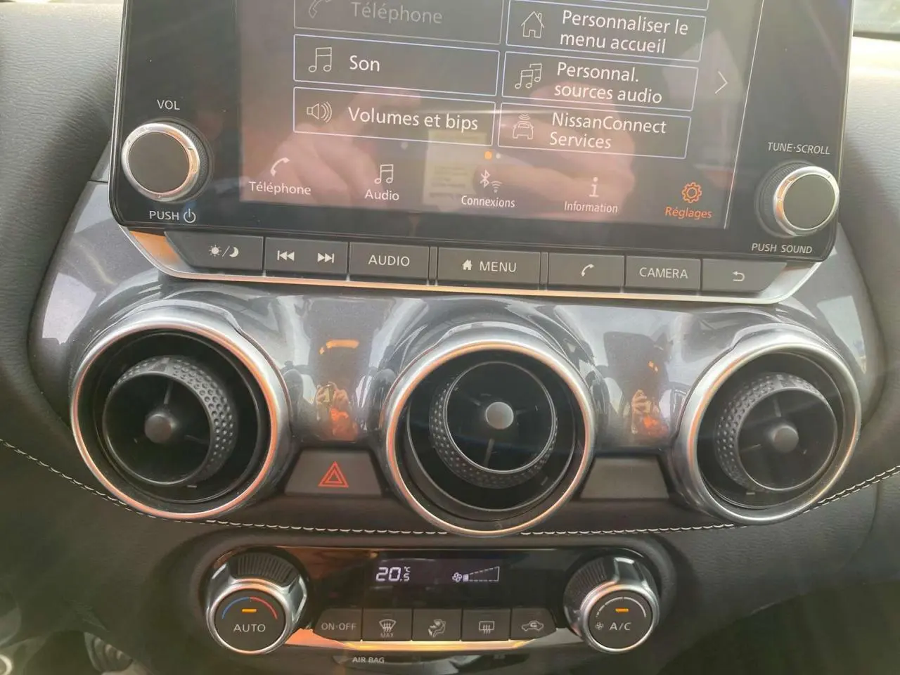 Vue rapprochée du tableau de bord du Nissan Juke blanc perle 2024, mettant en valeur l'écran tactile et les aérateurs ronds chromés.